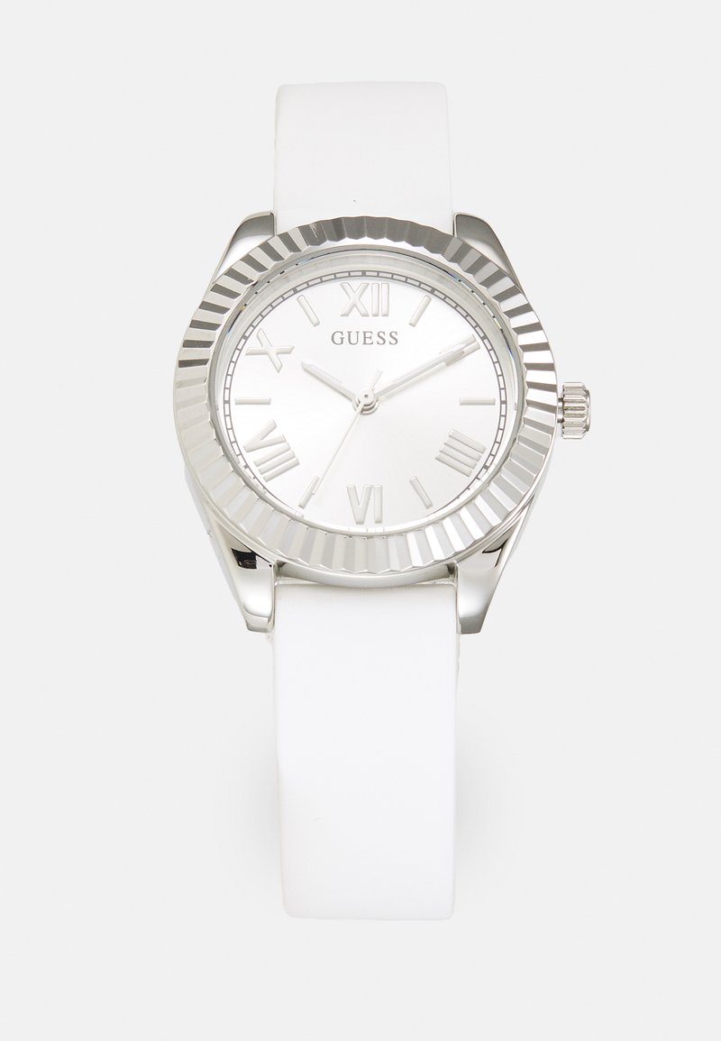 Silver watch with a white silicone strap, round face, textured bezel, and Roman numeral markers. Brand name "GUESS" displayed on dial.