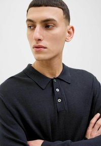 Marinblå polo skjorte laget av strikket stoff; har en klassisk krage, tre-knapps placket med grønne detaljer og synlige sømmer.