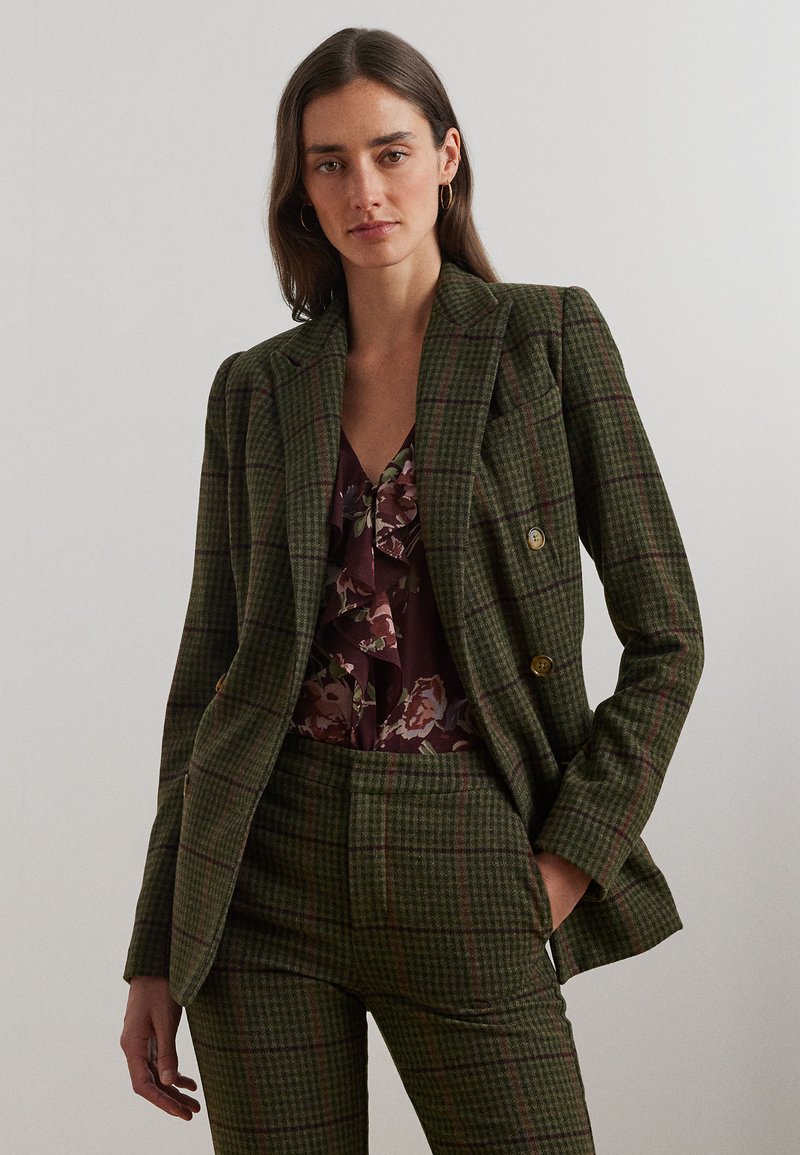 Groen geruite blazer met een dubbele knoopsluiting, gouden knopen en bijpassende broek. Daaronder een bordeauxkleurige bloemen-top met franje.