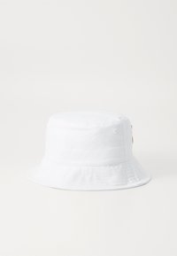 Chapéu bucket branco feito de tecido macio, com uma coroa redonda, aba larga e um detalhe em metal dourado de lado. Textura suave e sem padrões.