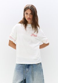 Hvid bomulds t-shirt med lyserøde stribede manchetter og rød kursiv "Stud." Rund hals, afslappet pasform, ensartet tekstur, velegnet til afslappet brug.