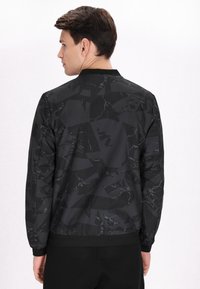 Giubbotto bomber nero con un motivo geometrico e riflessi lucidi. Realizzato in tessuto morbido, presenta un colletto e polsini a coste.