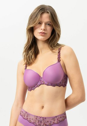 Jeune femme aux cheveux châtain clair portant un ensemble soutien-gorge et culotte lavande assorti avec un détail de broderie florale.