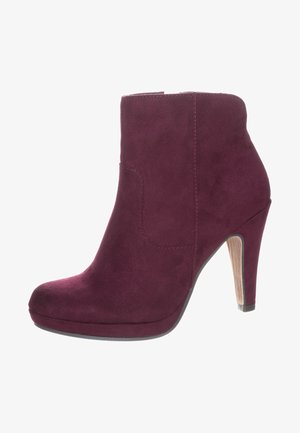 Pruimenkleurige suède enkellaars met een hoge stilettohak, ronde neus, zijrits en houten structuur op de hak.