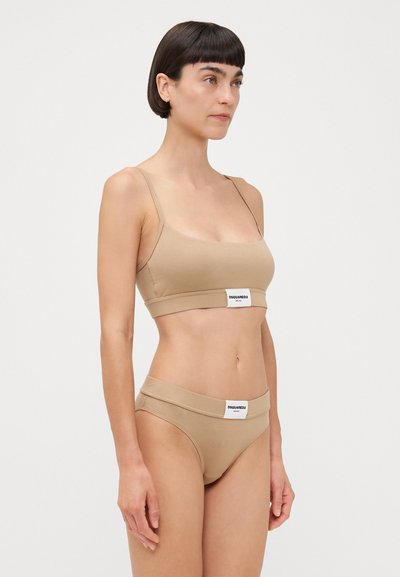 Nude-colored bralette and bikini set made of soft, stretchy material, featuring a wide band with a logo label on each piece.