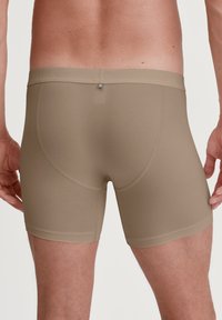 Boxer shorts beige con una texture liscia, cintura elastica e cucitura posteriore arrotondata, con un branding minimal vicino alla vita.