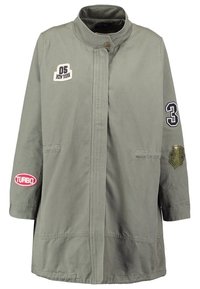 Abrigo largo de color verde olivo con cuello alzado, bolsillos frontales y parches que dicen "05 Nueva York", "3", "Turbo" y un emblema de camuflaje.