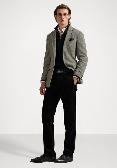 Siv hounds-tooth blazer preko črne jopice, v kombinaciji s črnimi kordnimi hlačami. Dodatki vključujejo očala in vzorčasto žepno rutico.