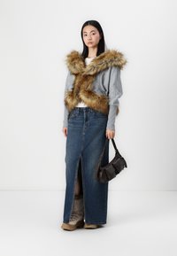 Γκρι πουλόβερ με καφέ ψεύτικο γούνινο γιακά, τζιν μακριά φούστα με μπροστινή σχισμή, καφέ τσάντα χειρός και καφέ μπότες με επένδυση από γούνα.