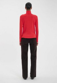 Haut rouge à col roulé côtelé associé à un pantalon noir aux jambes larges. Le tissu semble doux et la coupe est ajustée à la taille.