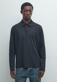 Dunkelgraues Poloshirt mit langen Ärmeln, Kragen und Dreiknopf-Leiste, kombiniert mit hellblauen Jeans.