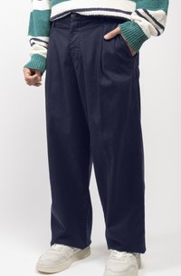 Pantalon large en marine avec une texture lisse, un devant plissé et des poches latérales, associé à des baskets de sport blanches.