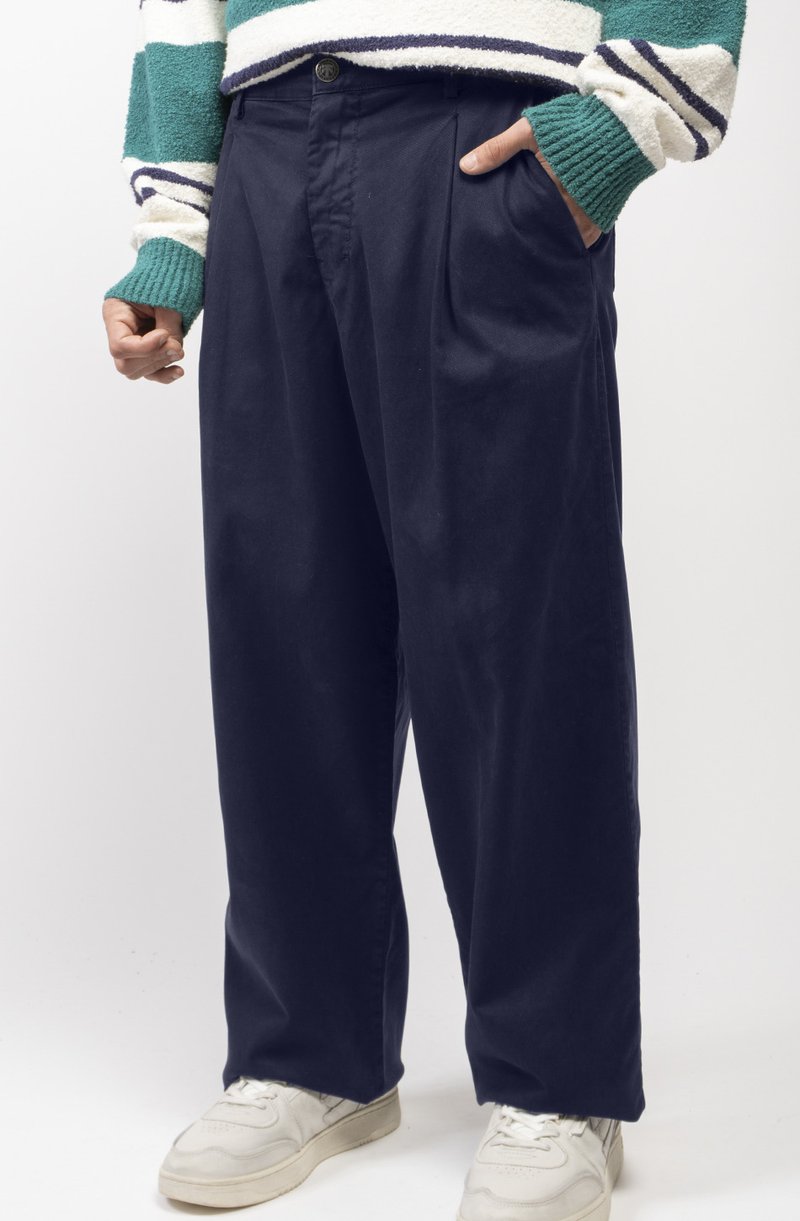 Pantalon large en marine avec une texture lisse, un devant plissé et des poches latérales, associé à des baskets de sport blanches.
