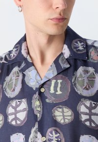 Camisa de mangas curtas com um fundo azul-marinho apresentando padrões circulares abstratos em cores suaves. Possui colarinho estilo camp e botões.