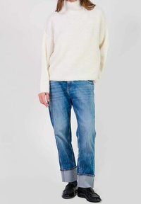 Kremowy sweter z golfem, o luźnym kroju, połączony z jasnoniebieskimi dżinsami z podwiniętymi nogawkami i czarnymi płaskimi butami.