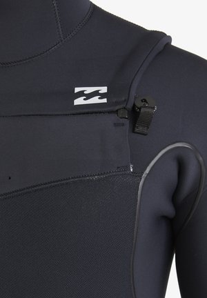 Close-up of black wetsuit with textured chest panel, zipper pull tab, and white wave logo on the upper chest area.