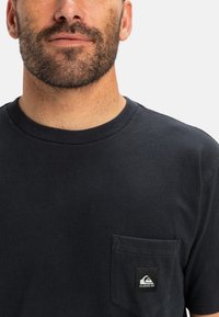 Navy blue cotton t-shirt with a crew neckline and short sleeves. Features a pocket on the left chest with a Quiksilver logo label.