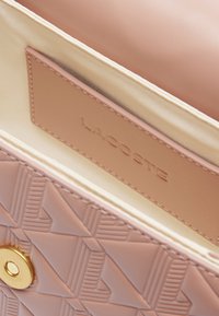 Intérieur de sac à main texturé rose avec une fermeture à pression dorée et une étiquette de marque en relief. Doublure lisse d'une couleur neutre claire.