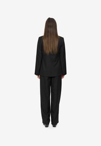 Zwarte pak bestaande uit een tailor-made jasje en losse broek, gezien vanuit de achterkant. Gladde textuur en standaard reversontwerp.