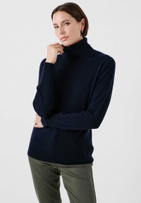 Jersey de cuello alto azul marino hecho de tela suave, con mangas largas y un corte relajado. Llevado con pantalones verde oliva. Diseño sencillo, sin patrones.