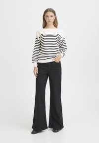 Pull-over à rayures bleu marine et crème, avec un col bateau, accompagné d'un pantalon noir évasé taille haute. Texture du tissu lisse.