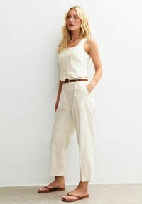 Mono de rayas blancas con parte superior ajustada y pantalones de pierna ancha, con botones en la parte delantera y un cinturón marrón. Textura suave y diseño informal.