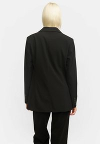 Mustat bleiserit, joissa on tarkka istuvuus, jämäkät olkapäät, yksittäinen takaventti ja napitettu hihansuu. Suuri, sileä kangas matta pinnalla.