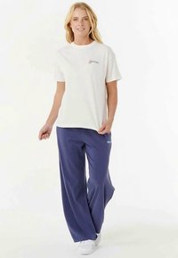 T-shirt blanc avec un petit logo, associé à un pantalon large bleu marine. Tissu texturé, coupe décontractée, porté avec des baskets blanches.