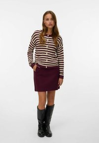Cardigan a righe con maglia crema e bordeaux, dotato di bottoni tondeggianti. Abbinato a una gonna bordeaux unita e stivali neri fino al ginocchio.