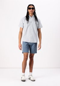 Chemise à manches courtes rayée en blanc et bleu, associée à un short bleu clair. Des chaussures de sport blanches avec des accents noirs complètent la tenue.