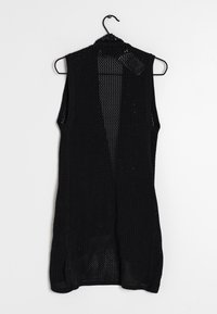 Černý bezrukávový kardigán vyrobený z otevřeného pleteného materiálu. Má V-krk a přímý střih s bočními rozparky, zavěšený na háčku.