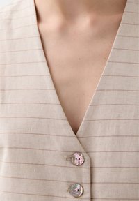Beige linnen vest met lichtbruine strepen, met een V-hals ontwerp en twee ronde, iriserende knopen aan de voorkant.