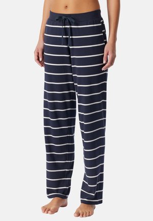 Pantalon de pyjama bleu marine avec des rayures blanches horizontales et une taille à cordon, porté par une personne debout, visible de mi-torse jusqu'aux pieds.