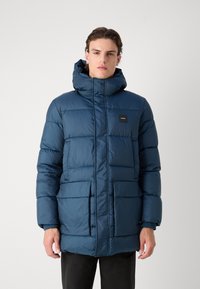 Parka blu gonfiabile con colletto alto, tasche frontali e una patch con logo. Il tessuto ha una superficie liscia e lucida, progettata per calore e comfort.