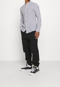 Gestreepte, langharige button-up blouse in blauw en wit, gecombineerd met zwarte cargobroek en zwart-witte sneakers met een gevoerde kraag.