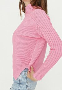Maglione rosa chiaro con collo alto, trama a coste e vestibilità leggermente oversize. L'orlo è appuntito con una cucitura laterale rilassata.