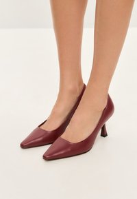 Scarpe con tacco alto in pelle borgogna, con punta affusolata e tacco a blocco inclinato; texture liscia e lati scanalati per un design elegante.