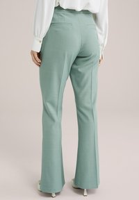 Pantalones acampanados color verde menta con una textura suave; presenta dos bolsillos en la parte trasera y una cintura de altura media, combinados con una blusa blanca suelta.