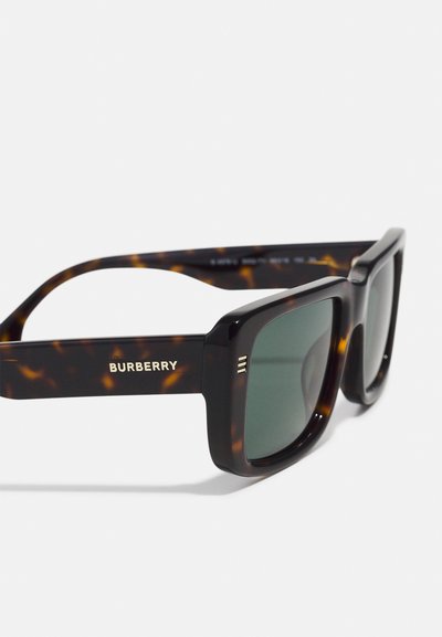 Gli occhiali da sole tartarugati Burberry presentano lenti verdi, montature quadrate audaci e il logo dorato sulle tempie, con tre linee parallele come dettagli decorativi.
