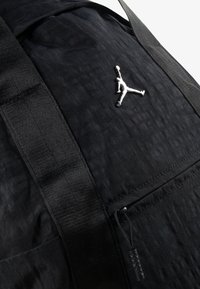 Crna leđa torba s teksturiranom tkaninom, sadrži srebrni Jumpman logo, podesive naramenice i džep s patentnim zatvaračem.