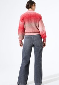 Brede, gebreide trui in verloop van roze naar grijs, met een gestructureerd patroon, een aansluitende taille en wijde, lange mouwen, gecombineerd met grijze jeans.