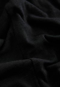 Tissu noir avec une surface douce et texturée, affichant de légers plis et un tombé fluide. Le matériau semble léger et polyvalent.