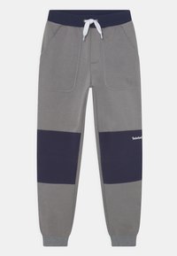 Szare dresy z granatowym poziomym panelem. Zawierają boczne kieszenie oraz elastyczny pas z regulowanym sznurkiem. Miękka, teksturowana tkanina.