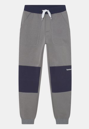 Graue Jogginghose mit einem navy-farbenen horizontalen Einsatz. Verfügt über Seitentaschen und einen elastischen Bund mit verstellbarem Kordelzug. Weicher, strukturierter Stoff.