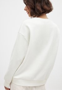 Weißer Sweatshirt mit lockerem Schnitt, fallenden Schultern und gerippten Bündchen. Weiche Textur und schlichtes Design, von hinten betrachtet.