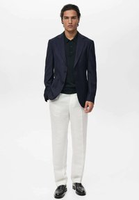 Granatowa marynarka, czarny polo i kremowe spodnie. Marynarka ma dwa guziki i kieszenie z klapkami; spodnie są proste. Czarne loafersy dopełniają całość.