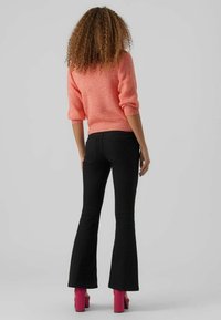 Zwarte flared jeans met een gebogen tailleband, gecombineerd met een koraalkleurige trui van breiwerk. De outfit wordt compleet gemaakt met roze blokhak schoenen.