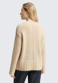 Beżowy sweter z dzianiny o luźnym kroju, z prążkowanym wykończeniem na dole i mankietach, z teksturowaną przędzą oraz szwem środkowym z tyłu.