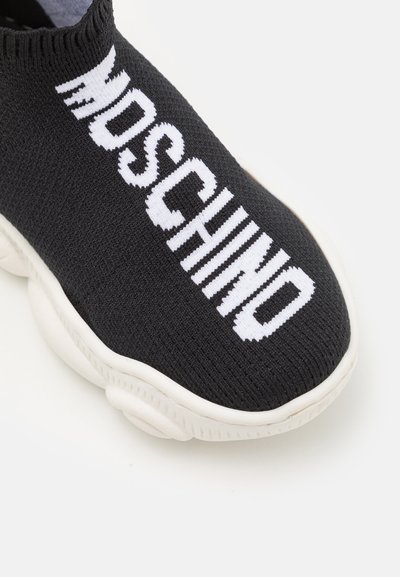 Black knit sneaker with white sole featuring bold white "MOSCHINO" text across the top front section.