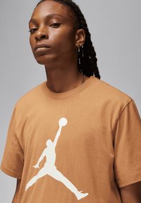 T-shirt in cotone marrone con una grande silhouette bianca di un giocatore di basket in aria. Collo rotondo e maniche corte.